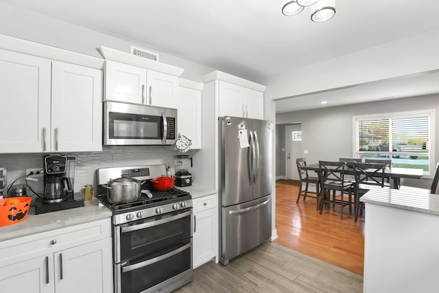 kitchen featuring light stone counters, white cabinets, tasteful backsplash, stainless steel appliances, and light hardwood / wood-style floors