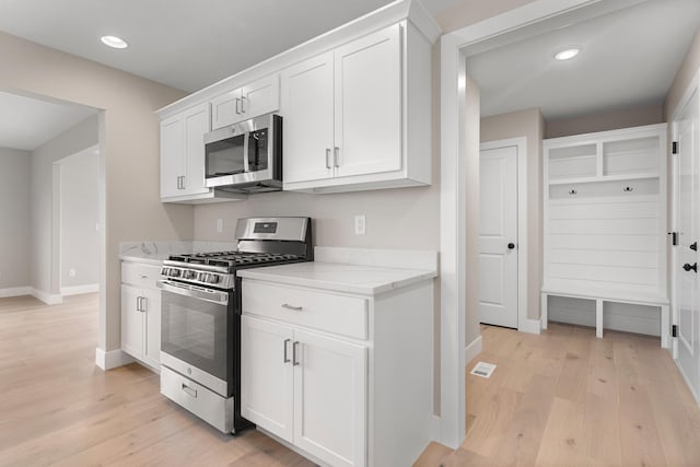 kitchen with light stone counters, white cabinets, stainless steel appliances, and light hardwood / wood-style floors