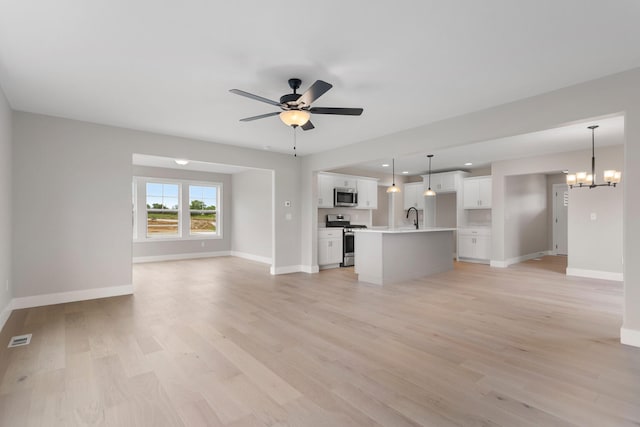 unfurnished living room with light wood-type flooring, ceiling fan with notable chandelier, and sink