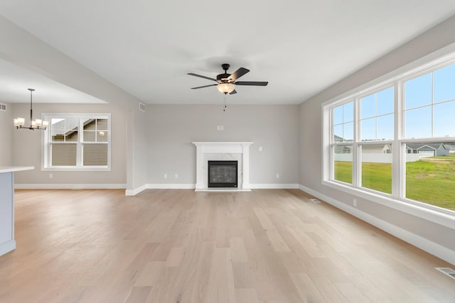 unfurnished living room with a premium fireplace, light hardwood / wood-style flooring, a healthy amount of sunlight, and ceiling fan with notable chandelier