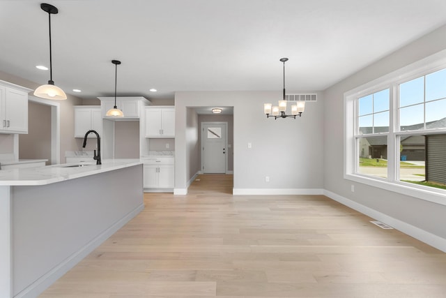 kitchen featuring sink, white cabinets, decorative light fixtures, and light wood-type flooring