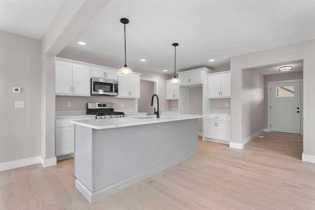 kitchen with stainless steel appliances, a center island with sink, white cabinets, light hardwood / wood-style floors, and hanging light fixtures