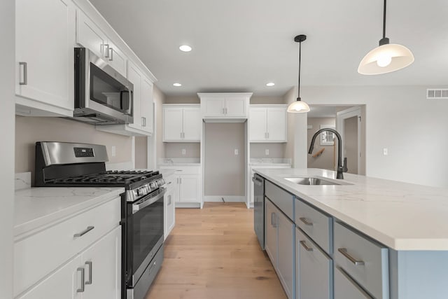 kitchen featuring white cabinetry, sink, hanging light fixtures, appliances with stainless steel finishes, and light wood-type flooring