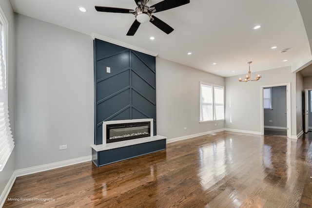 living room with ceiling fan with notable chandelier and dark hardwood / wood-style flooring