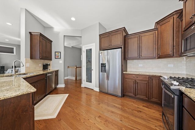 kitchen featuring sink, light stone counters, stainless steel appliances, light hardwood / wood-style floors, and backsplash