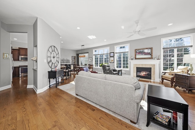 living room with a tiled fireplace, wood-type flooring, and ceiling fan