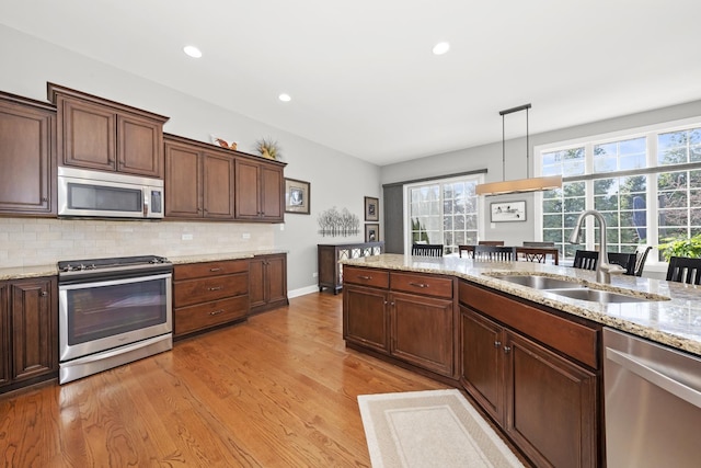 kitchen featuring sink, appliances with stainless steel finishes, pendant lighting, light stone countertops, and light hardwood / wood-style floors