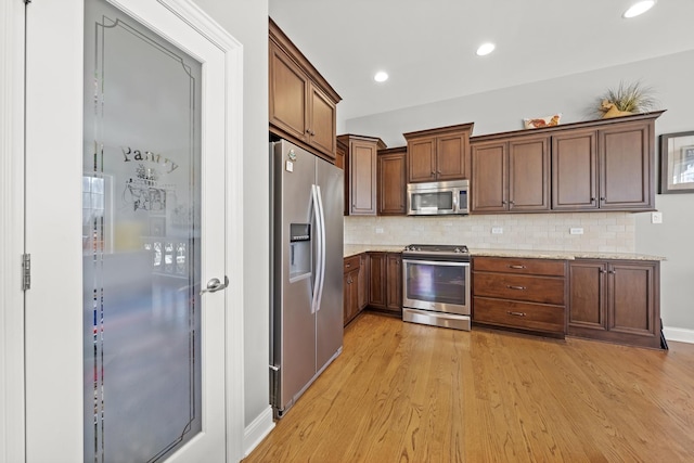 kitchen with decorative backsplash, light stone countertops, light hardwood / wood-style floors, and appliances with stainless steel finishes