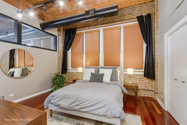 bedroom featuring dark hardwood / wood-style floors, brick wall, and track lighting