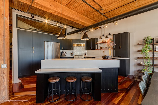 kitchen featuring an island with sink, hanging light fixtures, beam ceiling, high end fridge, and decorative backsplash