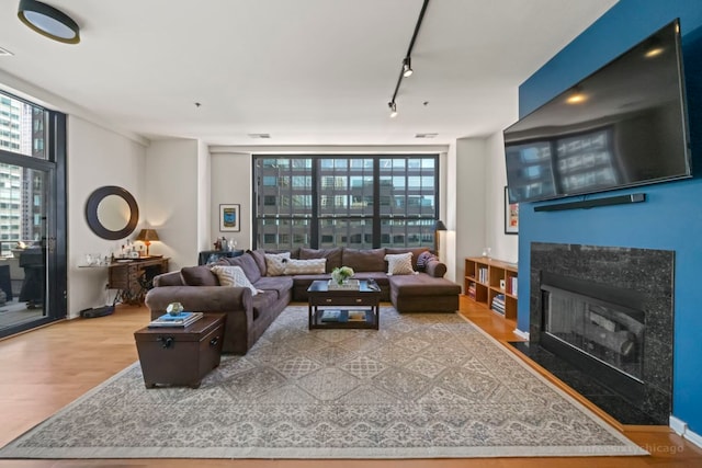 living room featuring wood-type flooring, a wall of windows, track lighting, and a high end fireplace