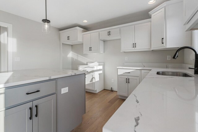 kitchen featuring light stone countertops, light wood-type flooring, sink, white cabinets, and hanging light fixtures