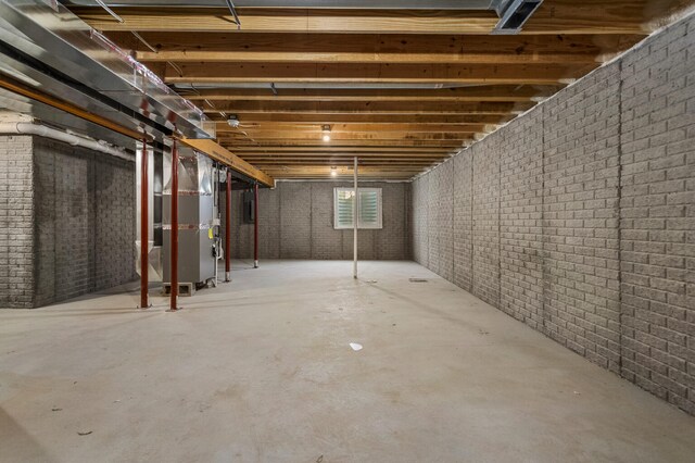 basement featuring electric water heater, brick wall, and heating unit