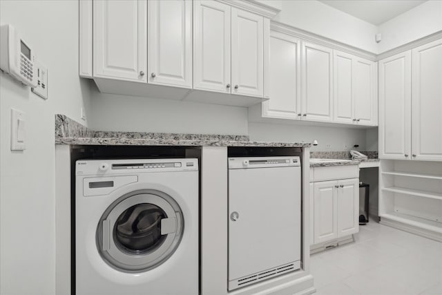 laundry area featuring washing machine and dryer, light tile patterned floors, and cabinets