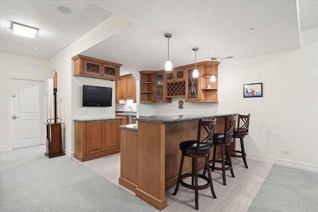 kitchen with sink, kitchen peninsula, decorative light fixtures, dark stone countertops, and a breakfast bar area