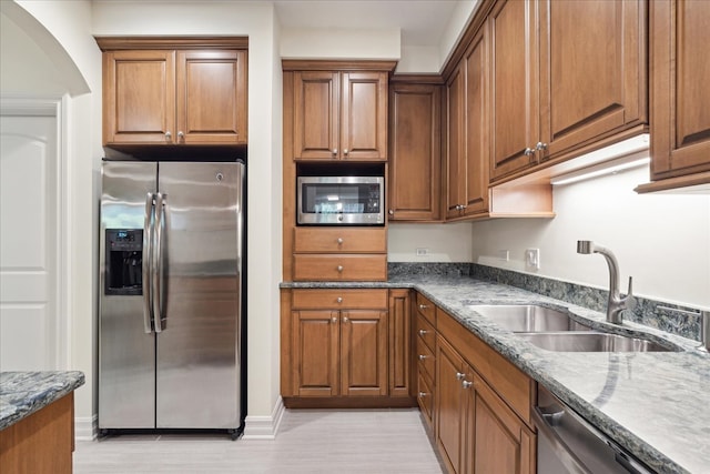 kitchen featuring dark stone countertops, stainless steel appliances, sink, and light wood-type flooring