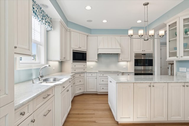 kitchen with stainless steel appliances, pendant lighting, custom exhaust hood, white cabinets, and light hardwood / wood-style flooring