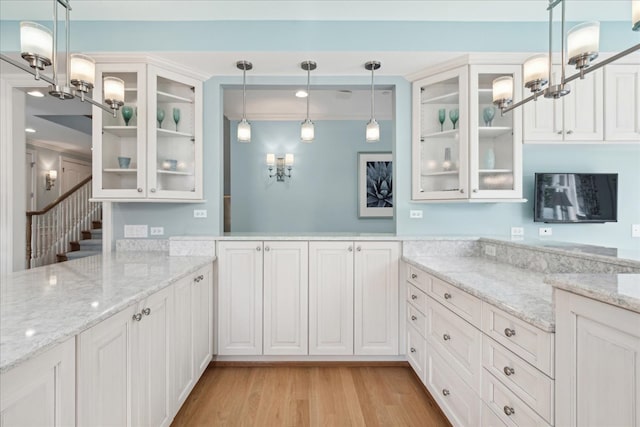 kitchen featuring light wood-type flooring, hanging light fixtures, white cabinetry, light stone counters, and ornamental molding