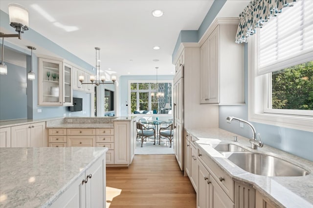 kitchen featuring light stone countertops, sink, pendant lighting, light hardwood / wood-style flooring, and a chandelier