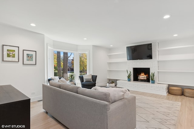 living room featuring built in features, light wood-type flooring, and a fireplace