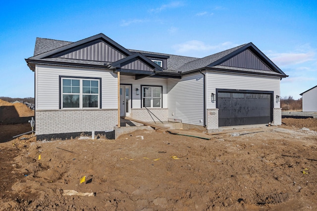 view of front of property featuring board and batten siding, an attached garage, brick siding, and roof with shingles