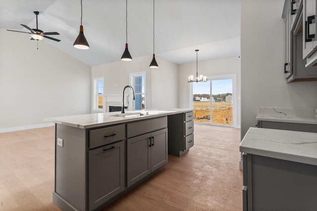 kitchen featuring gray cabinetry, a kitchen island with sink, ceiling fan with notable chandelier, a sink, and vaulted ceiling