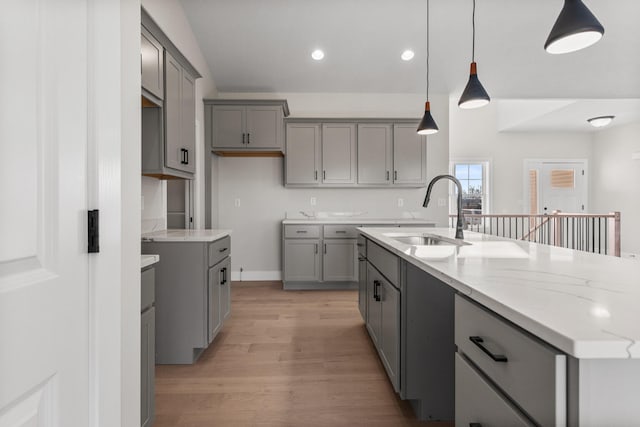 kitchen featuring a sink, light stone counters, light wood-style floors, and gray cabinets