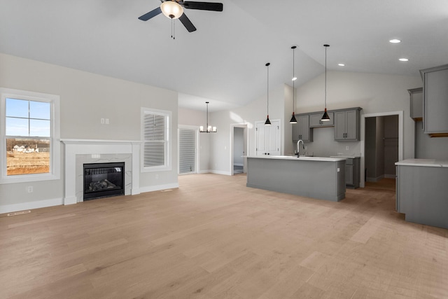 unfurnished living room featuring a premium fireplace, ceiling fan with notable chandelier, light wood-style floors, and a sink