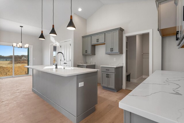 kitchen featuring light wood-style flooring, gray cabinets, a center island with sink, a sink, and an inviting chandelier