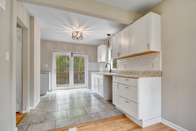 kitchen featuring white cabinets, hanging light fixtures, sink, light wood-type flooring, and decorative backsplash