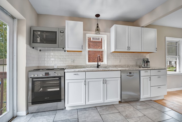 kitchen with white cabinets, sink, pendant lighting, appliances with stainless steel finishes, and backsplash