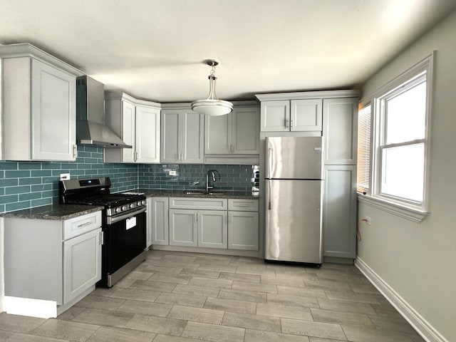 kitchen featuring wall chimney range hood, decorative light fixtures, sink, white cabinets, and appliances with stainless steel finishes