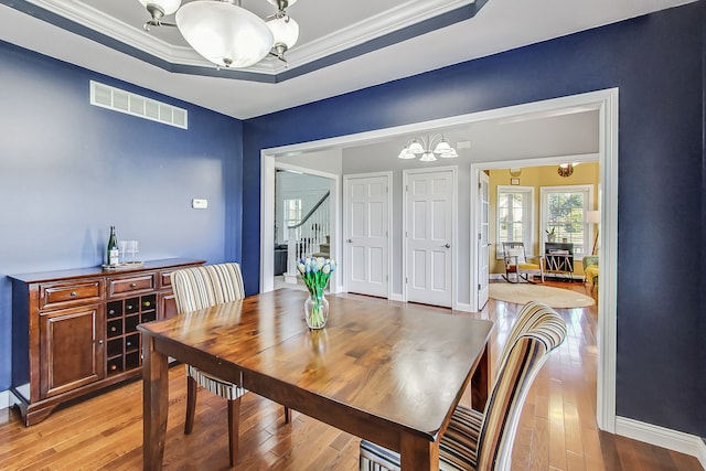 dining area with a notable chandelier, a raised ceiling, crown molding, and light hardwood / wood-style floors