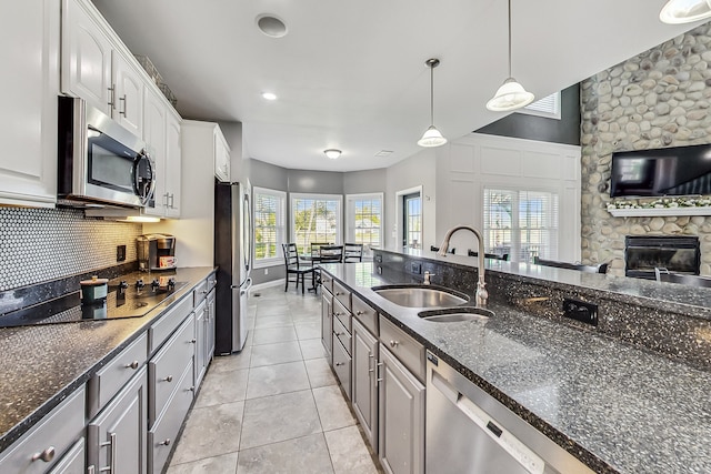 kitchen with sink, a fireplace, hanging light fixtures, white cabinets, and appliances with stainless steel finishes