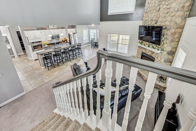 stairway with a stone fireplace, a towering ceiling, and carpet flooring