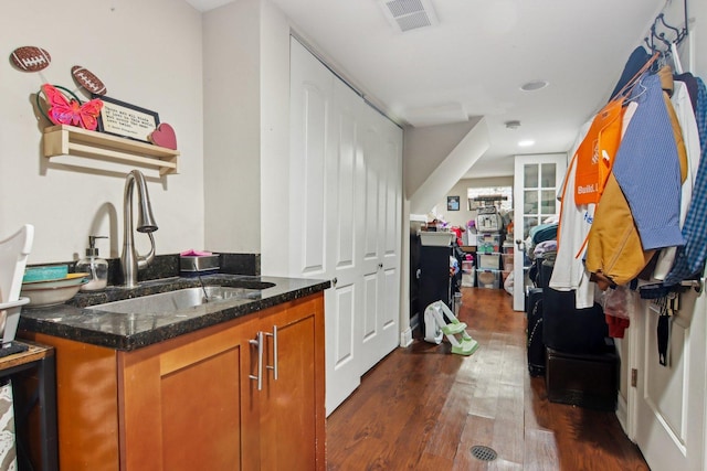 bar with dark wood-type flooring, sink, and dark stone countertops