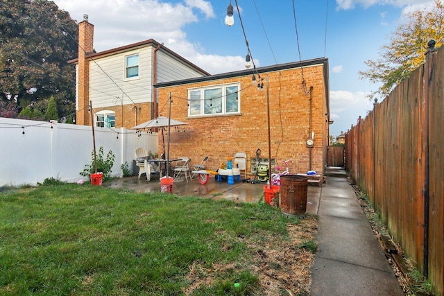 rear view of property featuring a patio area, a yard, a fenced backyard, and brick siding