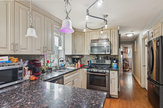 kitchen with decorative backsplash, appliances with stainless steel finishes, cream cabinets, wood finished floors, and a sink