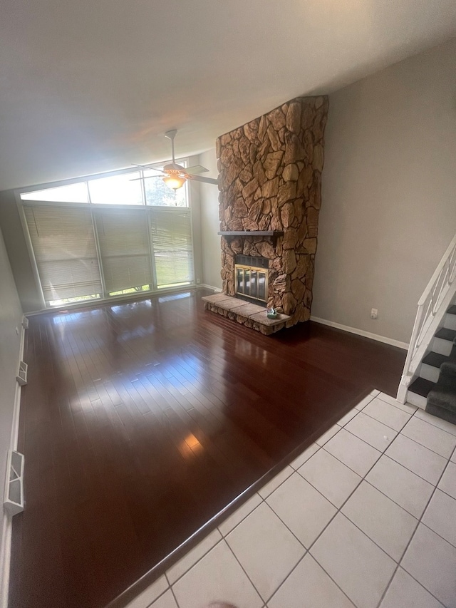 unfurnished living room with ceiling fan, a stone fireplace, and light wood-type flooring