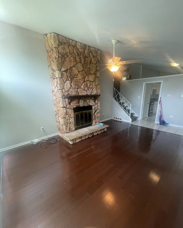 unfurnished living room featuring vaulted ceiling, ceiling fan, a stone fireplace, and wood-type flooring