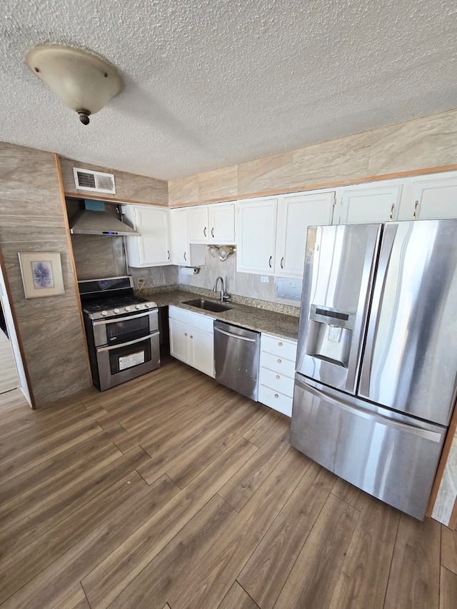 kitchen featuring wall chimney range hood, appliances with stainless steel finishes, sink, white cabinetry, and dark wood-type flooring