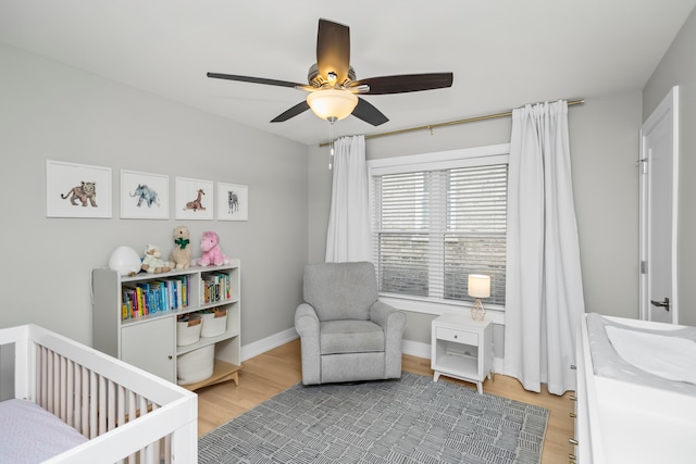 bedroom featuring ceiling fan, a crib, and wood-type flooring