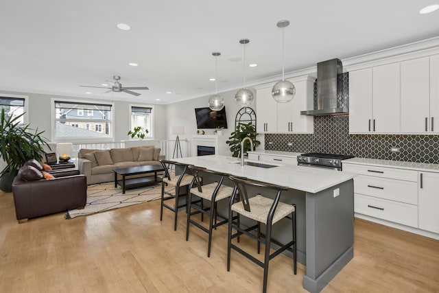 kitchen with white cabinets, decorative light fixtures, a kitchen island with sink, wall chimney exhaust hood, and a breakfast bar