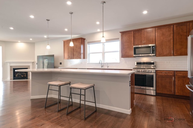 kitchen with appliances with stainless steel finishes, decorative light fixtures, dark wood-type flooring, and a kitchen island