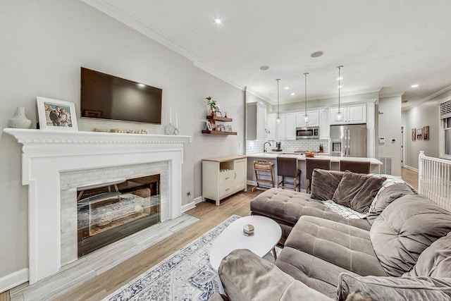 living room with a brick fireplace, light wood-type flooring, sink, and crown molding