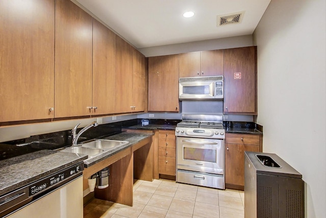 kitchen with appliances with stainless steel finishes, light tile patterned floors, dark stone counters, and sink