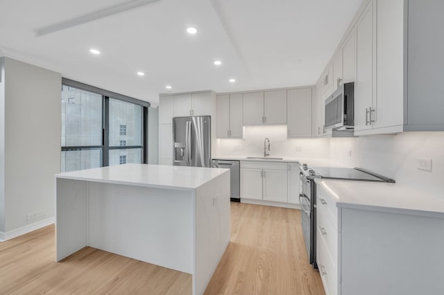 kitchen featuring appliances with stainless steel finishes, sink, a kitchen island, light hardwood / wood-style floors, and white cabinets