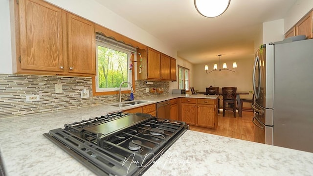 kitchen featuring light wood-type flooring, sink, a chandelier, appliances with stainless steel finishes, and decorative light fixtures