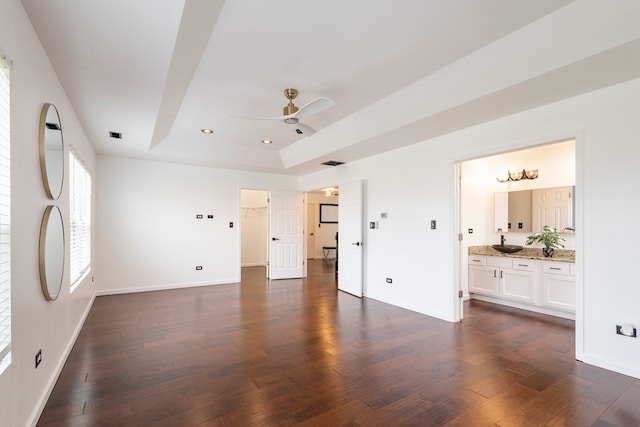 interior space featuring connected bathroom, dark wood-type flooring, a raised ceiling, and ceiling fan