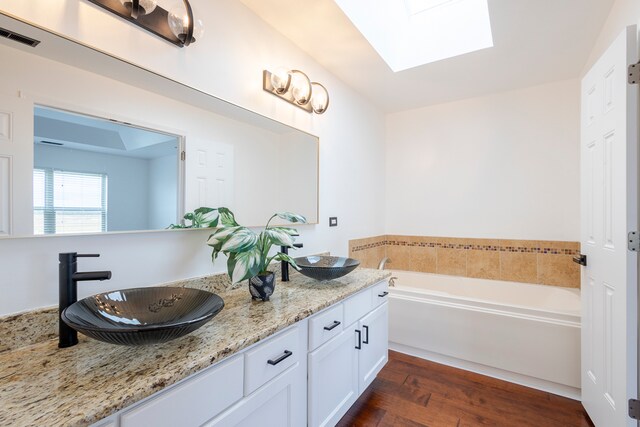 bathroom with vanity, a tub, hardwood / wood-style flooring, and a skylight